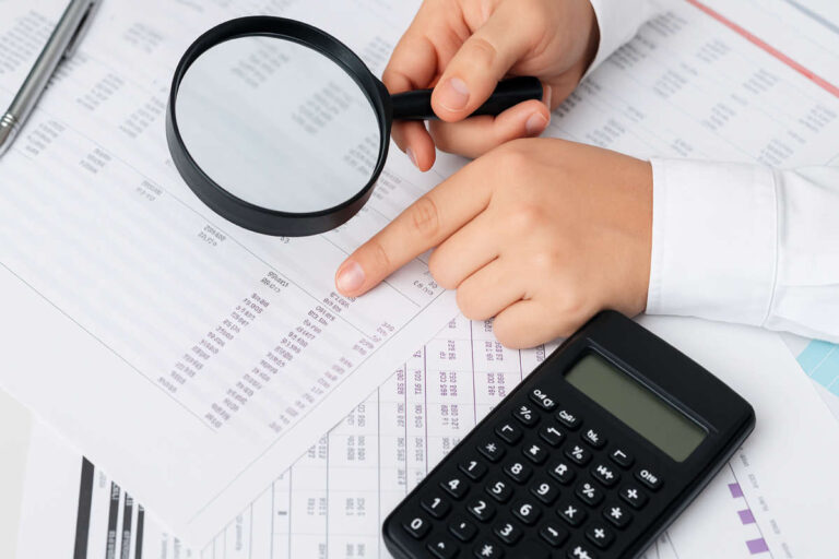 Primo piano di documenti contabili esaminati con lente di ingrandimento e calcolatrice, concetto di bilancio non certificato e verifica dei numeri.